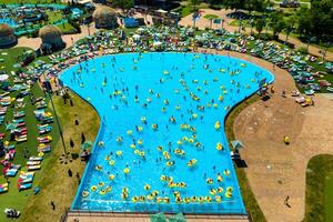 top visie van mensen ontspannende in de zwembad Aan geel opblaasbaar cirkels en zon bedden Aan de strand foto