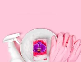 wasmiddel, keuken spons, roze rubber handschoenen, zeepachtig bord en orchidee bloem Aan de roze achtergrond. plat leggen. top visie. kopiëren ruimte. foto