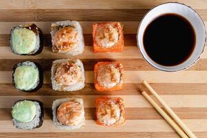 reeks van sushi broodjes Aan bamboe portie dienblad. uramaki rollen, eetstokjes en soja saus. foto