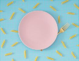 modieus voedsel patroon gemaakt van pasta penne rigate, roze bord en gouden vork Aan wit en blauw achtergrond. minimaal voedsel concept. creatief pasta patroon achtergrond. vlak leggen, top van visie. foto