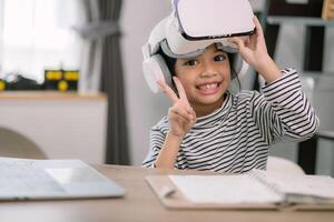 schattig Aziatisch weinig meisje vervelend vr bril met een laptop geplaatst Aan de tafel in stam technologie klas. online onderwijs. eruditie. foto