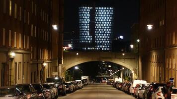 een straat in de centrum van Stockholm gedurende de nacht. van een afstand u kan zien de lichten van een modern gebouw. foto