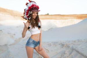 een mooi jong Kaukasisch meisje in een wit top en denim korte broek. Aan haar hoofd vervelend een Indisch hoed kakkerlak. staand in de woestijn. foto