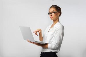 een streng bedrijf dame in bril en coördineren kantoor kleren is Holding een laptop in haar handen en demonstratief richten Bij hem met haar vinger foto