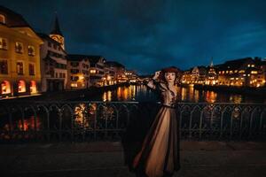 een elegant bruid in een zwart bruiloft jurk en rood hoed poses Bij nacht in de oud stad van Zürich. portret van een model- meisje na zonsondergang.foto schieten in Zwitserland. foto