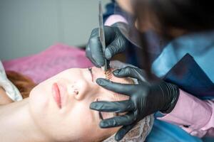 procedure van wenkbrauw microblading. een meester in zwart handschoenen is aan het doen een mengen naald- van model's voorhoofd. foto