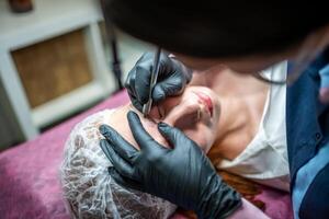 procedure van wenkbrauw microblading. een meester in zwart handschoenen is aan het doen een mengen naald- van model's voorhoofd. foto