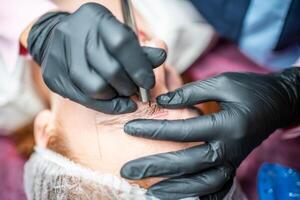 procedure van wenkbrauw microblading. een meester in zwart handschoenen is aan het doen een mengen naald- van model's voorhoofd. foto