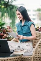 jong vrouw Holding credit kaart en gebruik makend van Tablet. een glimlachen jong vrouw bezighoudt met een tablet temidden van levendig groen gebladerte. online winkelen, e-commerce, internet bankieren, uitgeven geld. foto