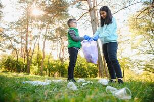 vrouw vrijwilliger en weinig jongen plukken omhoog de plastic vuilnis en zetten het in biologisch afbreekbaar vuilniszak buitenshuis. ecologie, recycling en bescherming van natuur concept. milieu bescherming. foto