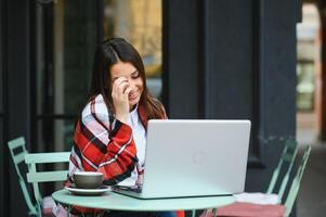 jong, een meisje in een buitenshuis cafe met een laptop pratend door een video telefoontje met iemand, aipi telefonie foto