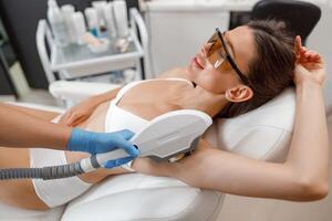 vrouw cliënt in bril gedurende oksel foto epileren procedure met ipl machine in schoonheid salon