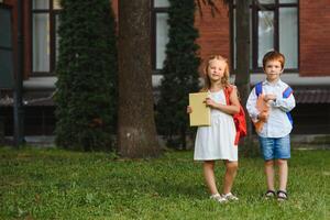 twee leerlingen van primair school. jongen en meisje met school- Tassen achter de rug. begin van school- lessen. warm dag van val. terug naar school. weinig eerste klassers. foto