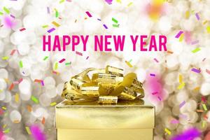 gelukkig nieuwjaarswoord met gouden geschenkdoos met lint en kleurrijke confetti bij onscherpte gouden boekh foto