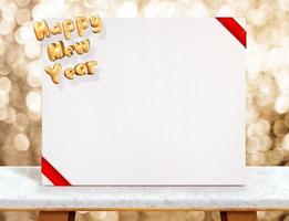 gelukkig nieuwjaar op witte poster met rood lint op marmeren tafel bij gouden sprankelende bokeh-achtergrond foto