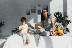 mam met zoon in pyjama aan het eten fruit Aan bed. portret Vrolijk, lachend, blij familie, moeder en zoon hebben ontbijt in bed, verrassing Aan mam dag. positief menselijk emoties foto