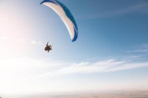 een paraglider met een blauw parachute vlieg. een mannetje vliegen Aan de lucht en liften een paraglider in de lucht foto