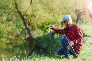 Mens ontspannende en visvangst door oever van het meer. weekends gemaakt voor vissen. visser mannelijk hobby. meester lokaas. houden kalmte en vis Aan. fishman gehaakt spinnen in de rivier- aan het wachten groot vis. vent vlieg visvangst foto