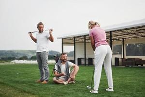 meisje golfen en slaan door putter op groen. haar leraar helpt om de techniek te verkennen en haar eerste aanvallen te maken foto