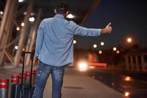 er rijdt een auto op de straatlijn. kortharige man in spijkerbroek en een shirt met bagage probeert de auto te vangen foto