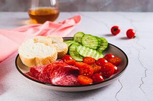 meisje avondeten van gerookt worst, komkommers, kers tomaten en broodjes Aan een bord Aan de tafel foto