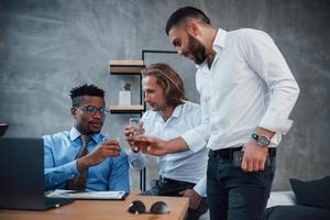 whisky drinken. groep multiraciale kantoormedewerkers in formele kleding praten over taken en plannen foto
