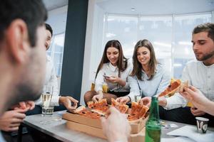 een goede tijd hebben. pizza eten. succesvolle deal vieren. jonge kantoormedewerkers zitten bij de tafel met alcohol foto