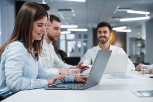 mensen hebben een zakelijk gesprek. zijaanzicht van meisje werkt op de zilverkleurige laptop op kantoor en lacht foto