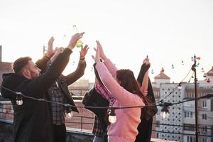 het is geluk. handen omhoog. jongeren brengen een zonnige herfstdag op het dak door met gitaar en drankjes foto