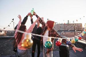 mensen maken een toast. vakantie op het dak. vrolijke groep vrienden stak hun hand op met alcohol foto