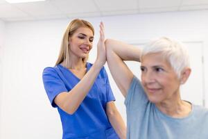 dokter of fysiotherapeut werken onderzoeken behandelen gewond arm van senior vrouw geduldig, uitrekken en oefening, aan het doen de revalidatie behandeling pijn in kliniek. foto