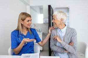 jong vrouw dokter of gp in wit medisch uniform raadplegen senior vrouw geduldig in privaat ziekenhuis. vrouw therapeut spreken praten met vrouw cliënt Aan overleg in kliniek. foto