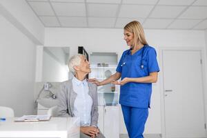 jong vrouw dokter of gp in wit medisch uniform raadplegen vrouw geduldig in privaat ziekenhuis. vrouw therapeut spreken praten met senior vrouw cliënt Aan overleg in kliniek. foto