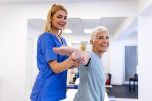 dokter orthopedische onderwijs senior vrouw naar Doen osteoporose behandeling oefening in modern kliniek. fysiotherapeut helpen vrouw geduldig gedurende spier revalidatie fysiotherapie foto