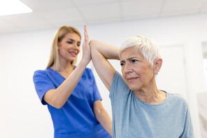 dokter orthopedische onderwijs senior vrouw naar Doen osteoporose behandeling oefening in modern kliniek. fysiotherapeut helpen vrouw geduldig gedurende spier revalidatie fysiotherapie foto