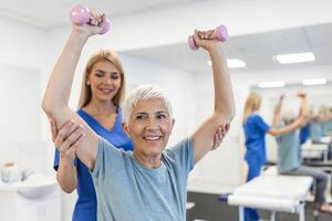 Oder oud vrouw aan het doen fysiotherapie met ondersteuning van fysiotherapeuten . senior ouderen vrouw zittend in kliniek gebruik makend van halters training oefening voor geduldig met verzorger in verpleging zorg. foto