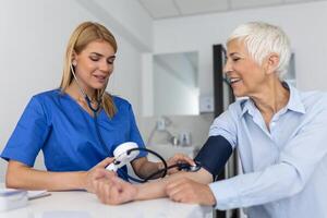 meten bloed druk. senior vrouw hebben een bezoek met vrouw dokter in modern kliniek. meten bloed druk. druk graadmeter. hypertensie en hoog hart tarief foto