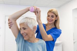 fysiotherapeut vrouw geven oefening met halter behandeling over arm en schouder van senior vrouw geduldig fysiek behandeling concept foto