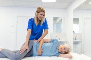 professioneel chiropractor of fysiotherapeut helpt naar genezen een senior vrouw rug. dokter reparaties de geduldig aan het liegen Aan een bankstel van een modern revalidatie kliniek concept van fysiek revalidatie. foto