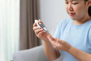 Aziatisch vrouw gebruik makend van lancet Aan vinger voor controle bloed suiker niveau door glucose meter, suikerziekte. foto