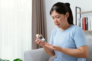 Aziatisch vrouw gebruik makend van lancet Aan vinger voor controle bloed suiker niveau door glucose meter, suikerziekte. foto