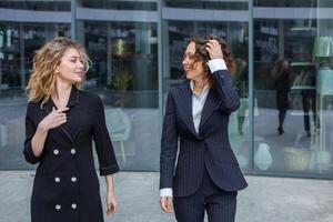 twee geslaagd bedrijf Dames zijn pratend in de stad in voorkant van een modern gebouw. bedrijf vergadering Aan de straat. 2 vrouw managers met top posities. foto