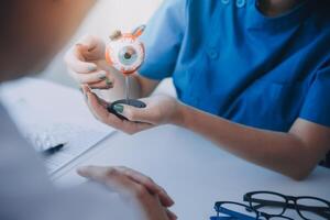 detailopname van Aziatisch vrouw dokter pratend met ouderen geduldig tonen oogbol model- en uitleggen oog ziekte in ziekenhuis foto