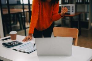 zakenvrouw of accountant werken financieel investering Aan rekenmachine, berekenen, analyseren bedrijf en afzet groei Aan financieel document gegevens grafiek, boekhouding, economisch, reclame concept. foto