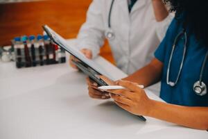 medisch arbeider in laboratorium jas en steriel masker, aan het doen een microscoop analyse terwijl haar collega zijn werken achter foto