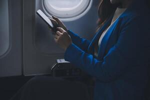 jong Aziatisch bedrijf vrouw pratend Aan smartphone, zakenvrouw werken terwijl vliegend Bij vlak, jong vrouw gebruik makend van de internet Bij vliegtuig, lucht reis, lang vlucht. foto
