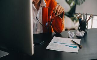 Aziatisch bedrijf vrouw gebruik makend van rekenmachine en laptop voor aan het doen wiskunde financiën Aan een kantoor bureau, belasting, rapport, boekhouding, statistieken, en analytisch Onderzoek concept foto