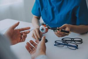 detailopname van Aziatisch vrouw dokter pratend met ouderen geduldig tonen oogbol model- en uitleggen oog ziekte in ziekenhuis foto