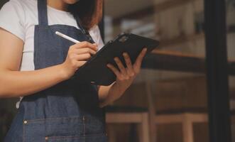 startup succesvolle kleine ondernemer mkb schoonheid meisje staan met tablet smartphone in coffeeshop restaurant. portret van aziatische tan vrouw barista café-eigenaar. MKB ondernemer verkoper bedrijfsconcept foto