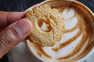 zoete koekjes gieten in een koffiemok op houten tafel foto